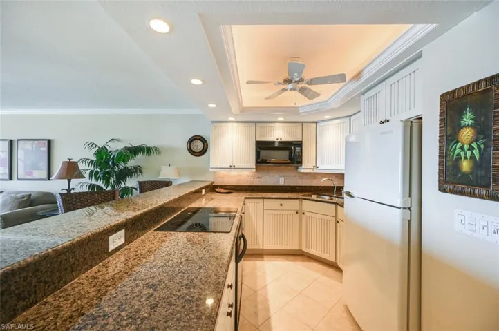 Kitchen with black appliances, a tray ceiling, sink, ceiling fan, and light tile patterned flooring
