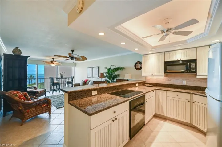 Kitchen featuring black appliances, dark stone countertops, a tray ceiling, kitchen peninsula, and ceiling fan