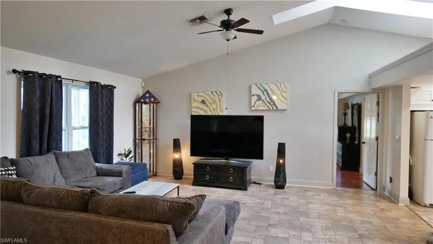 Living room featuring vaulted ceiling with skylight, ceiling fan, and light tile floors