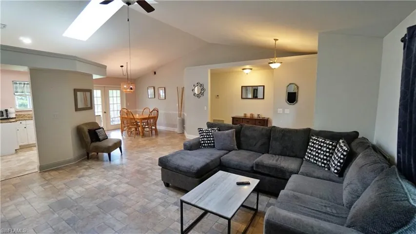 Living room featuring vaulted ceiling with skylight, light tile flooring, and ceiling fan