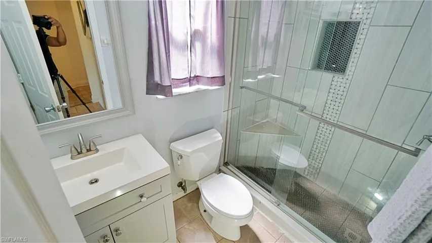 Bathroom with tile flooring, a shower with shower door, toilet, and large vanity