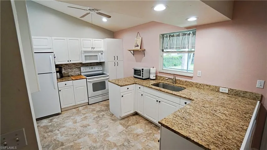 Kitchen featuring vaulted ceiling, kitchen peninsula, ceiling fan, sink, and white appliances