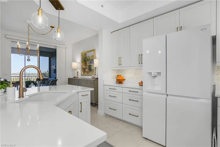 Kitchen with white refrigerator with ice dispenser, white cabinets, decorative light fixtures, backsplash, and light tile patterned floors