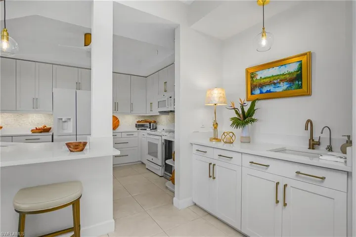 Kitchen featuring decorative light fixtures, white appliances, and light stone counters