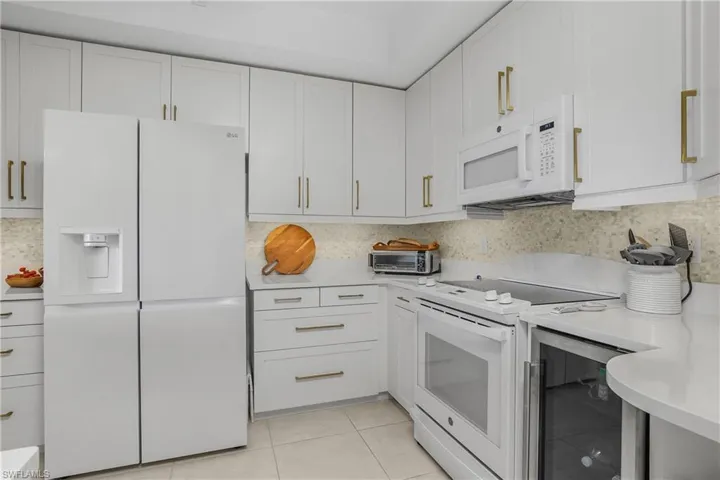 Kitchen with white appliances, beverage cooler, white cabinets, light tile patterned floors, and light stone counters