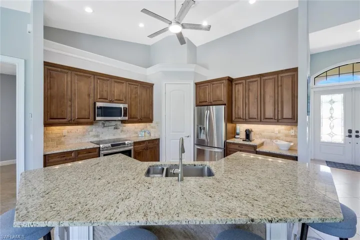 Kitchen featuring a kitchen breakfast bar, stainless steel appliances, a kitchen island with sink, a towering ceiling, and sink