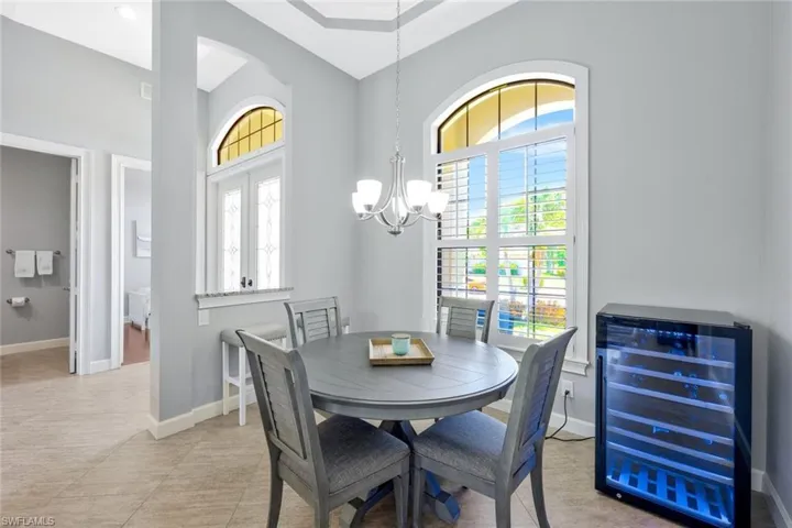 Dining space featuring a high ceiling, beverage cooler, light tile flooring, and a chandelier