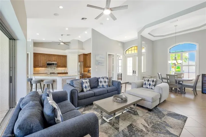 Tiled living room featuring a tray ceiling, high vaulted ceiling, and ceiling fan
