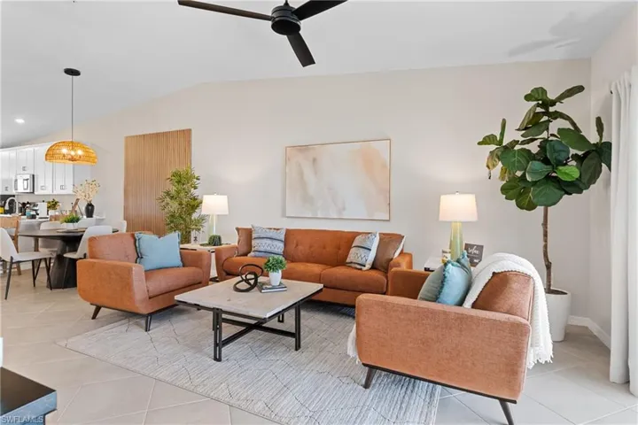 Living room with vaulted ceiling, light tile patterned floors, a ceiling fan, and a chandelier