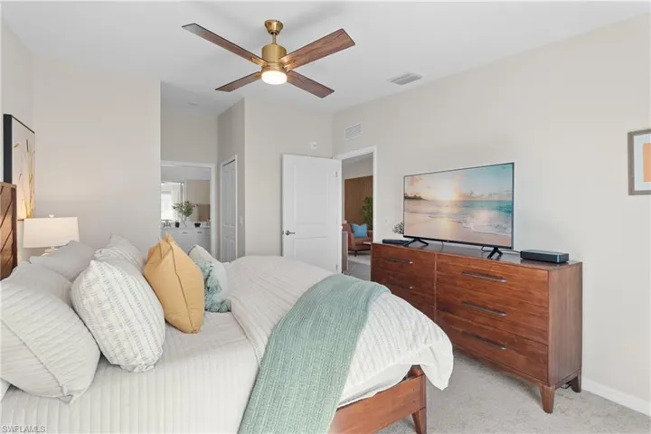 Bedroom featuring light colored carpet, ensuite bathroom, ceiling fan, and a closet