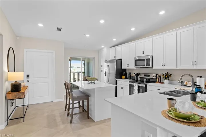 Kitchen with a breakfast bar area, stainless steel appliances, white cabinetry, a center island, and light stone countertops