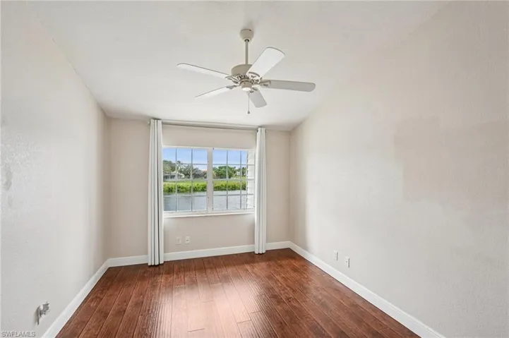 Unfurnished room featuring dark wood-style floors, a ceiling fan, a water view, and a textured wall