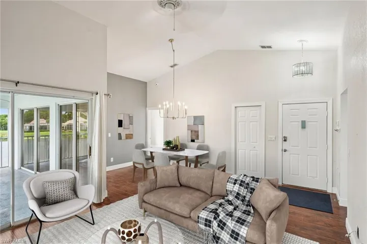Living area with high vaulted ceiling, a chandelier, wood finished floors, and a water view