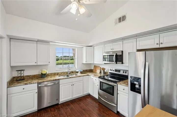 Kitchen with stainless steel appliances, white cabinetry, dark wood-style flooring, light stone countertops, and lofted ceiling
