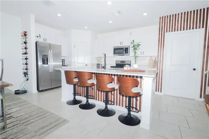 Kitchen featuring a breakfast bar area, stainless steel appliances, white cabinets, a center island with sink, and light stone counters