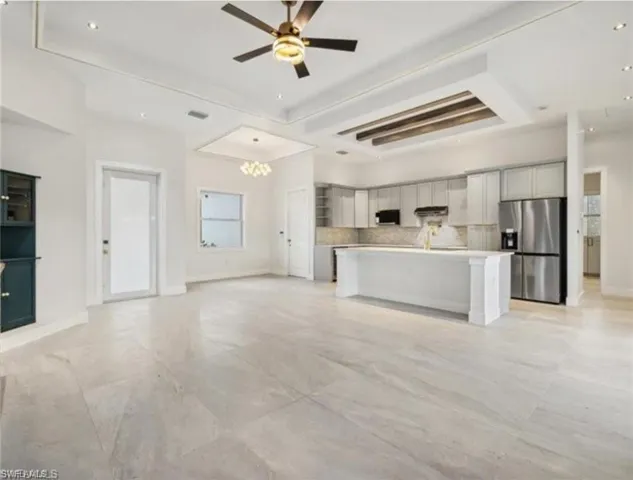 Kitchen featuring an island with sink, light countertops, stainless steel fridge, open floor plan, and ceiling fan with notable chandelier