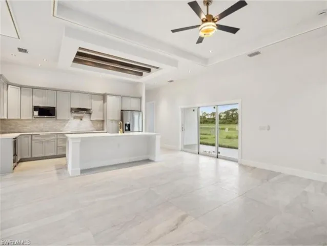 Unfurnished living room featuring attic access, baseboards, a ceiling fan, and visible vents
