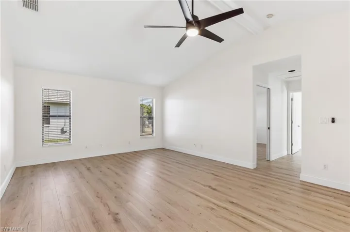 Spare room with lofted ceiling with beams, ceiling fan, light wood-style flooring, visible vents, and baseboards