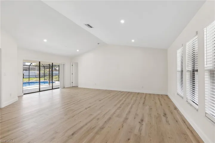 Empty room with vaulted ceiling, light wood finished floors, visible vents, and baseboards