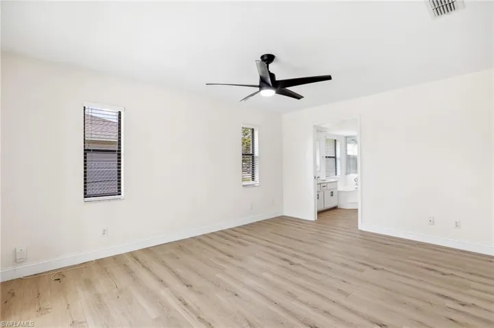 Unfurnished bedroom with baseboards, visible vents, a ceiling fan, ensuite bath, and light wood-type flooring