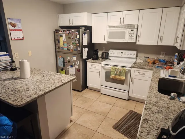 Kitchen featuring white appliances, light stone counters, and white cabinetry