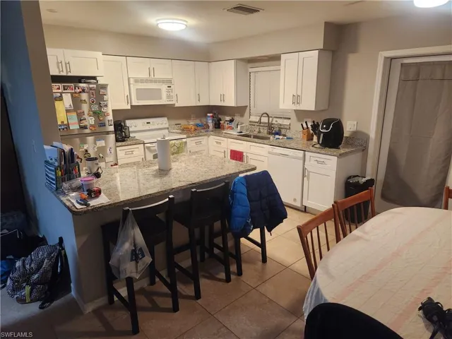 Kitchen featuring white cabinets, light stone counters, white appliances, and a kitchen bar