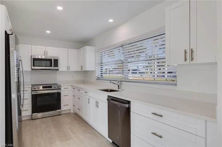 Kitchen featuring stainless steel appliances, white cabinets, light wood-style floors, recessed lighting, and light stone countertops