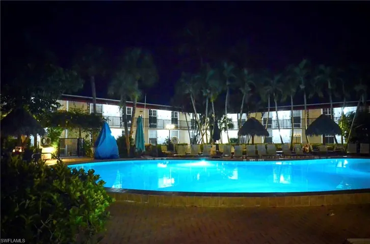 Resort-style outdoor pool with luminous blue water, surrounded by mature palm trees and lush landscaping