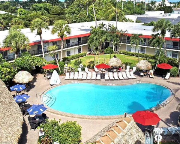 Resort-style pool area featuring a freeform swimming pool, surrounding lounge chairs, multiple thatched-roof palapas, and lush tropical landscaping