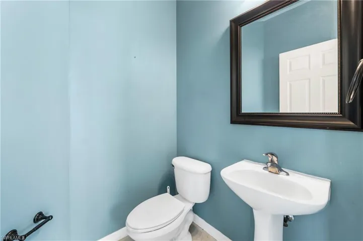 Bathroom featuring a pedestal sink, white toilet, and a framed mirror