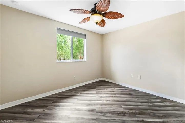 Room featuring wood-finish flooring, a white window frame, and a ceiling fan with leaf-shaped blades