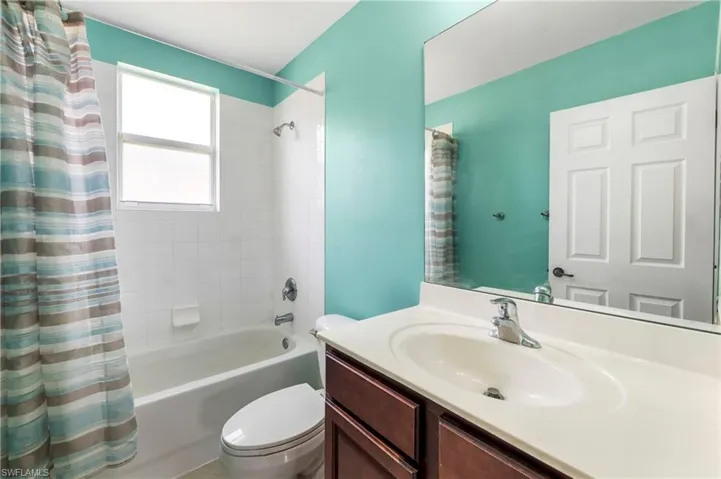Bathroom featuring a built-in vanity with an integrated sink, a large wall-mounted mirror, white ceramic tile shower surround, a full bathtub, and a window for natural light