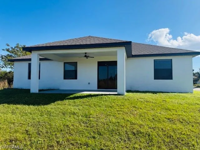 Back of house featuring ceiling fan, a patio, a yard, stucco siding, and roof with shingles