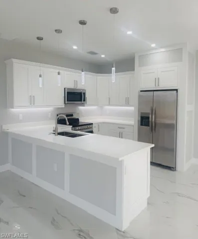 Kitchen featuring appliances with stainless steel finishes, white cabinetry, hanging light fixtures, a peninsula, and recessed lighting