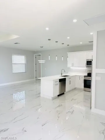 Kitchen with pendant lighting, white cabinets, stainless steel appliances, open floor plan, and a peninsula