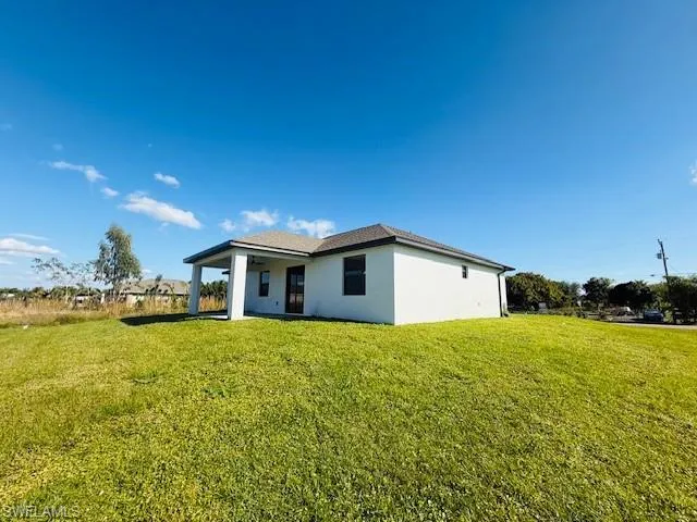 Rear view of property with a lawn, stucco siding, and a patio
