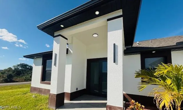 View of exterior entry featuring stucco siding and a yard