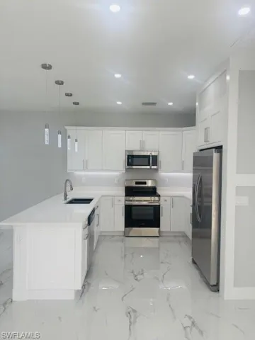 Kitchen with stainless steel appliances, light marble finish floors, hanging light fixtures, white cabinets, and recessed lighting