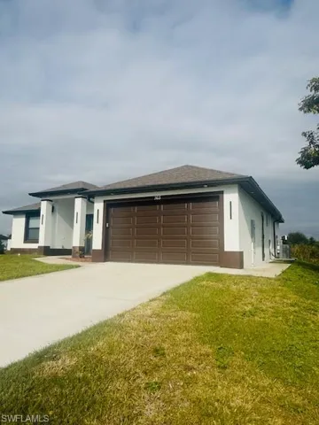 View of front of house featuring stucco siding, concrete driveway, a front lawn, and a garage