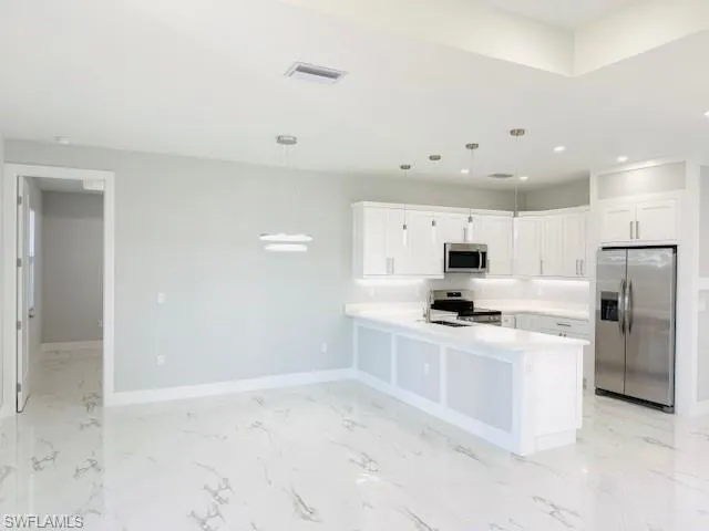 Kitchen featuring appliances with stainless steel finishes, light countertops, a peninsula, white cabinets, and pendant lighting