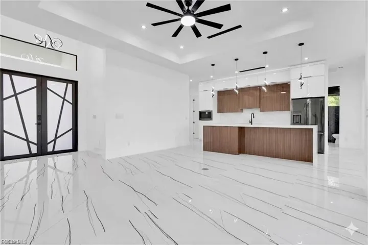Unfurnished living room featuring a ceiling fan, a tray ceiling, light marble finish flooring, recessed lighting, and french doors