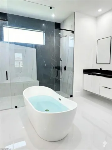Bathroom featuring a marble finish shower, a freestanding bath, and vanity