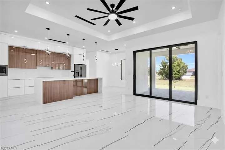 Unfurnished living room with a ceiling fan, light marble finish floors, a tray ceiling, and suspended lighting