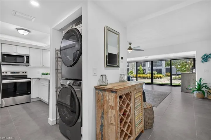 Sleek tile flooring throughout, full kitchen with stainless steel appliances and white cabinetry, stacked laundry appliances, and large sliding glass doors
