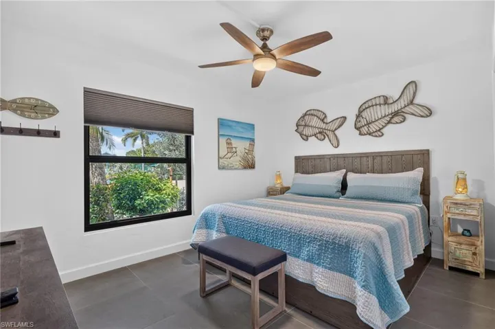 White walls featuring a window with integrated blinds, wood-finish ceiling fan, and dark tile flooring