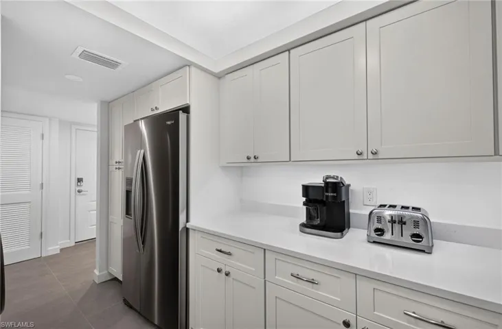 Stainless steel refrigerator, white shaker-style cabinetry, light-toned countertops, tile flooring, and recessed lighting