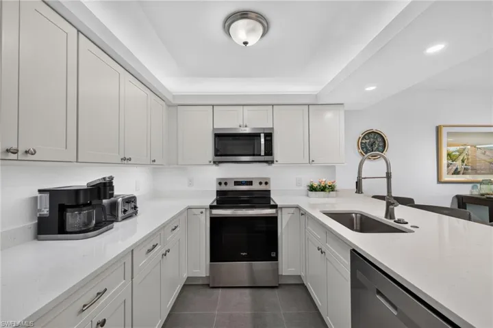 U-shaped kitchen featuring white cabinetry, light-toned countertops, stainless steel appliances, and an undermount sink with a gooseneck faucet