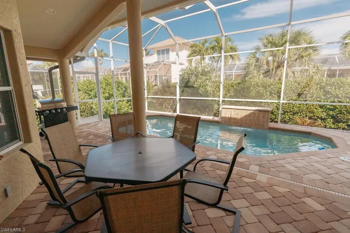 Outdoor covered dining area on back patio with grill and pool