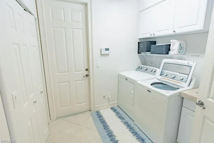 Laundry room featuring light tile patterned floors, washer and clothes dryer, and cabinet space