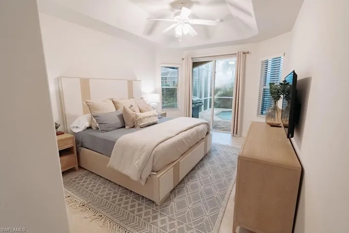 Spacious master Bedroom featuring a tray ceiling, ceiling fan, and access to back patio pool area